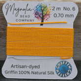 Yellow thread on a spool with 'Magnolia Bead Company' label on a wooden background